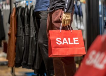 Part of male mannequin dressed in casual clothes holding the Sales paper shopping bag