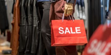 Part of male mannequin dressed in casual clothes holding the Sales paper shopping bag