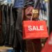 Part of male mannequin dressed in casual clothes holding the Sales paper shopping bag