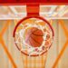From below shot of basketball ball falling through net in gym.