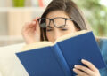 Woman suffering eyestrain trying to read a book at home
